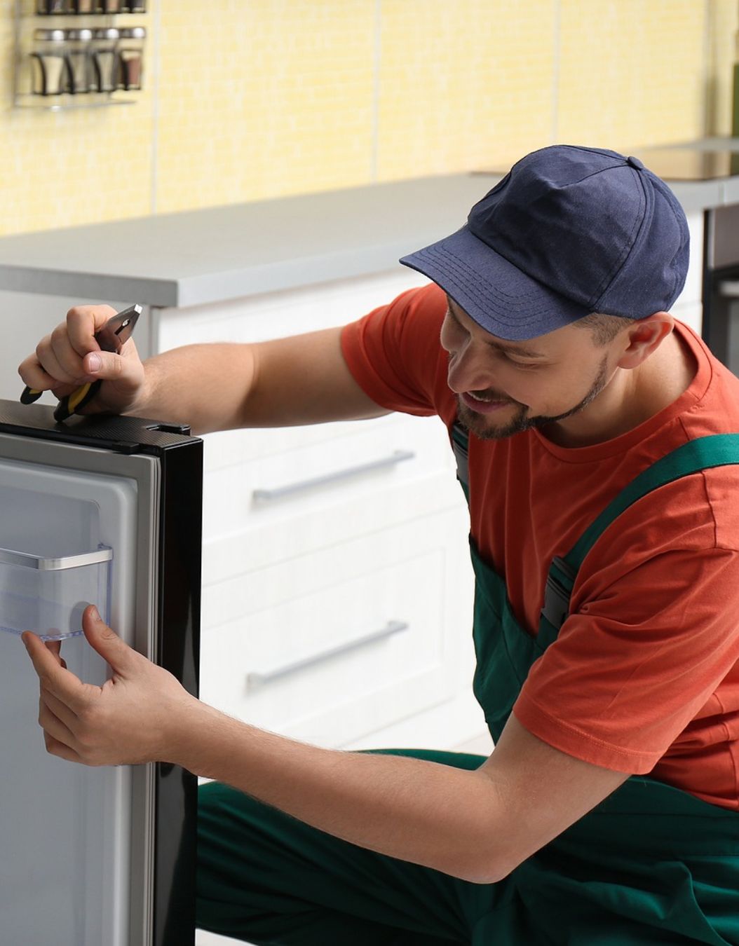 A man in overalls is engaged in refrigerator repair, emphasizing appliance repair services in Sacramento, CA.