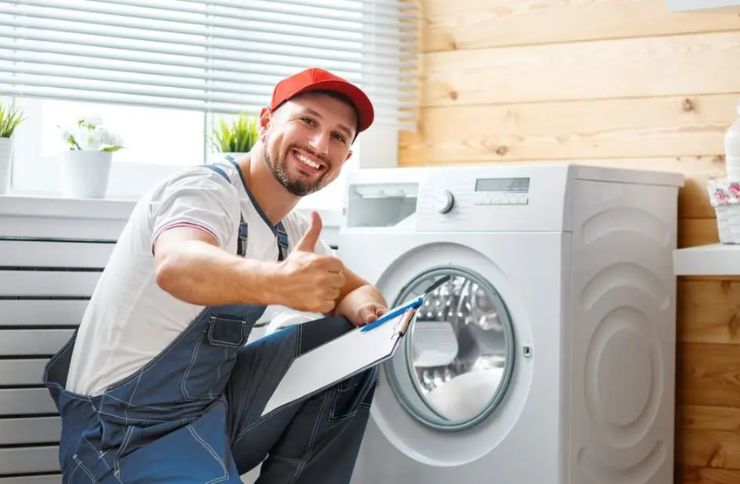 A man in overalls and a hat holds a clipboard and points at a washing machine, indicating laundry repair services in Sacramento.