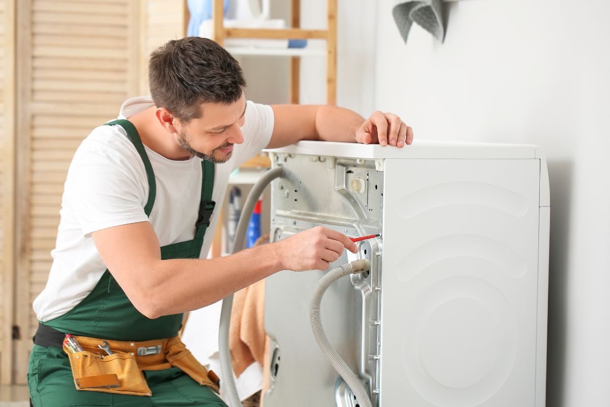 A man in an apron repairs a washing machine, demonstrating his skills in appliance maintenance and troubleshooting. 