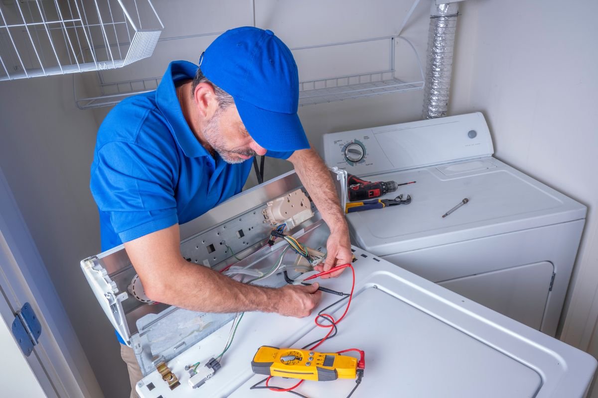 A man wearing a blue shirt is engaged in fixing a washing machine, demonstrating his technical skills.